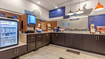 A modern breakfast area with a refrigerated display, a coffee machine, and a counter with various food items.