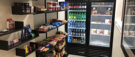 A self-service beverage and snack area with shelves stocked with various drinks, snacks, and personal care items.