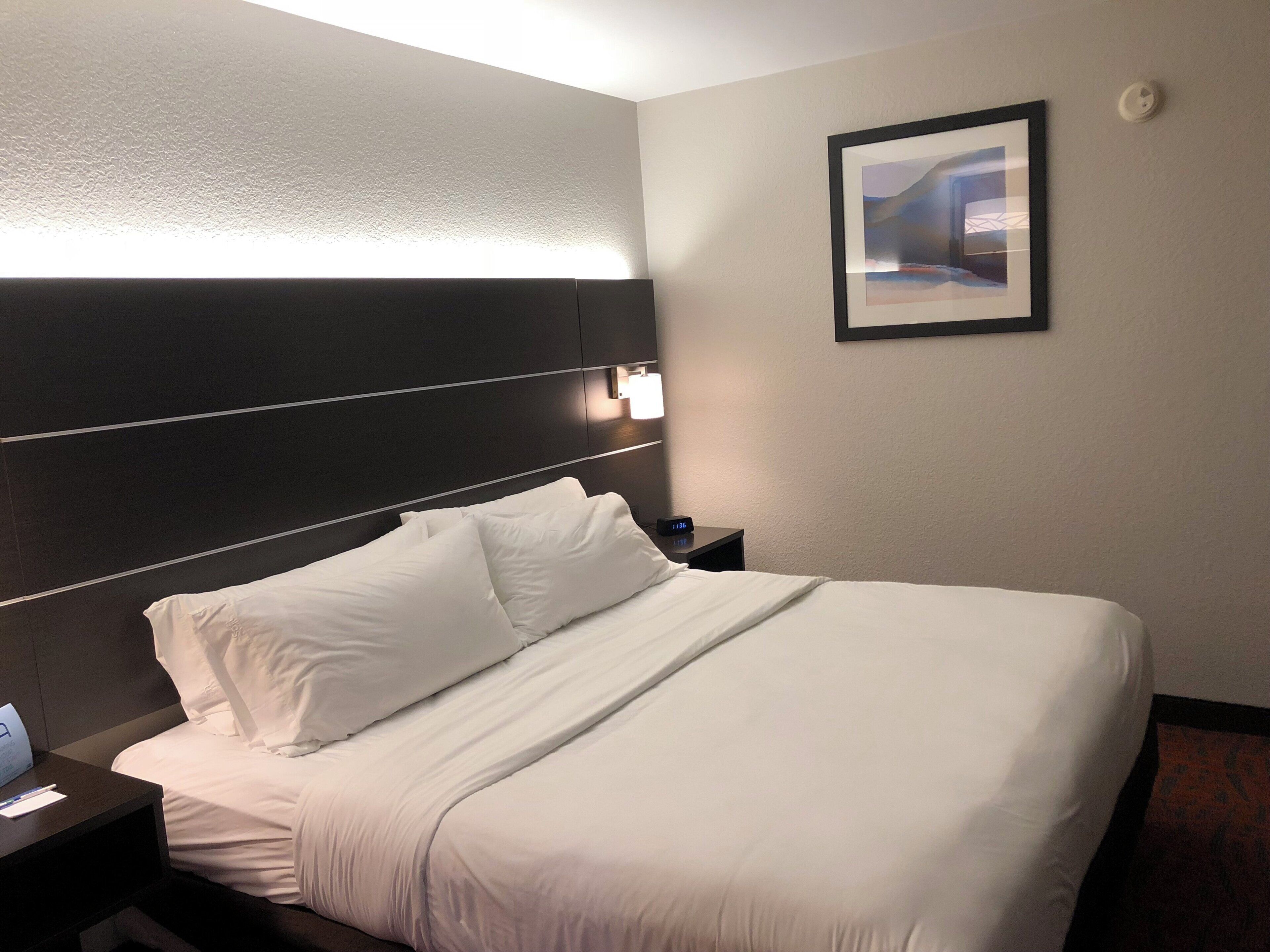 Una camera d'albergo con un letto grande, un comodino, una lampada a parete e un quadro appeso al muro.