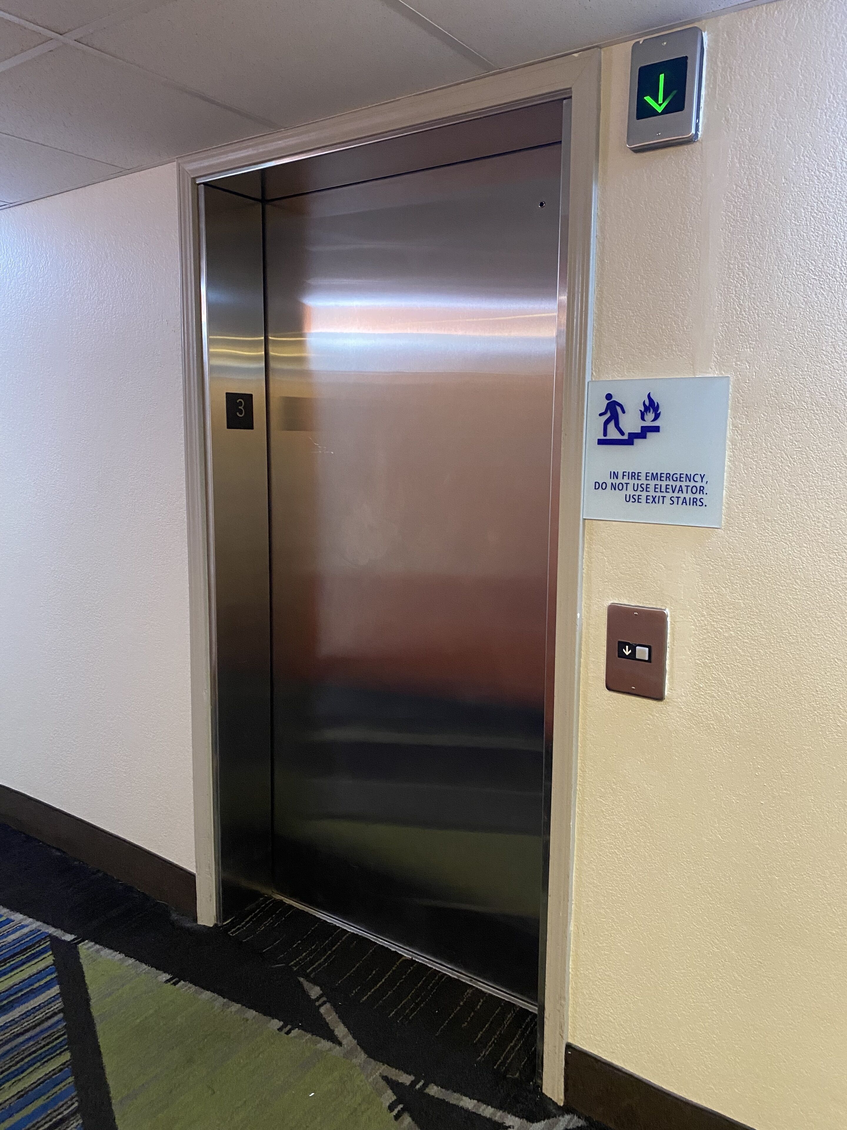 Ascensor con un cartel que indica usar las escaleras de emergencia en caso de incendio.