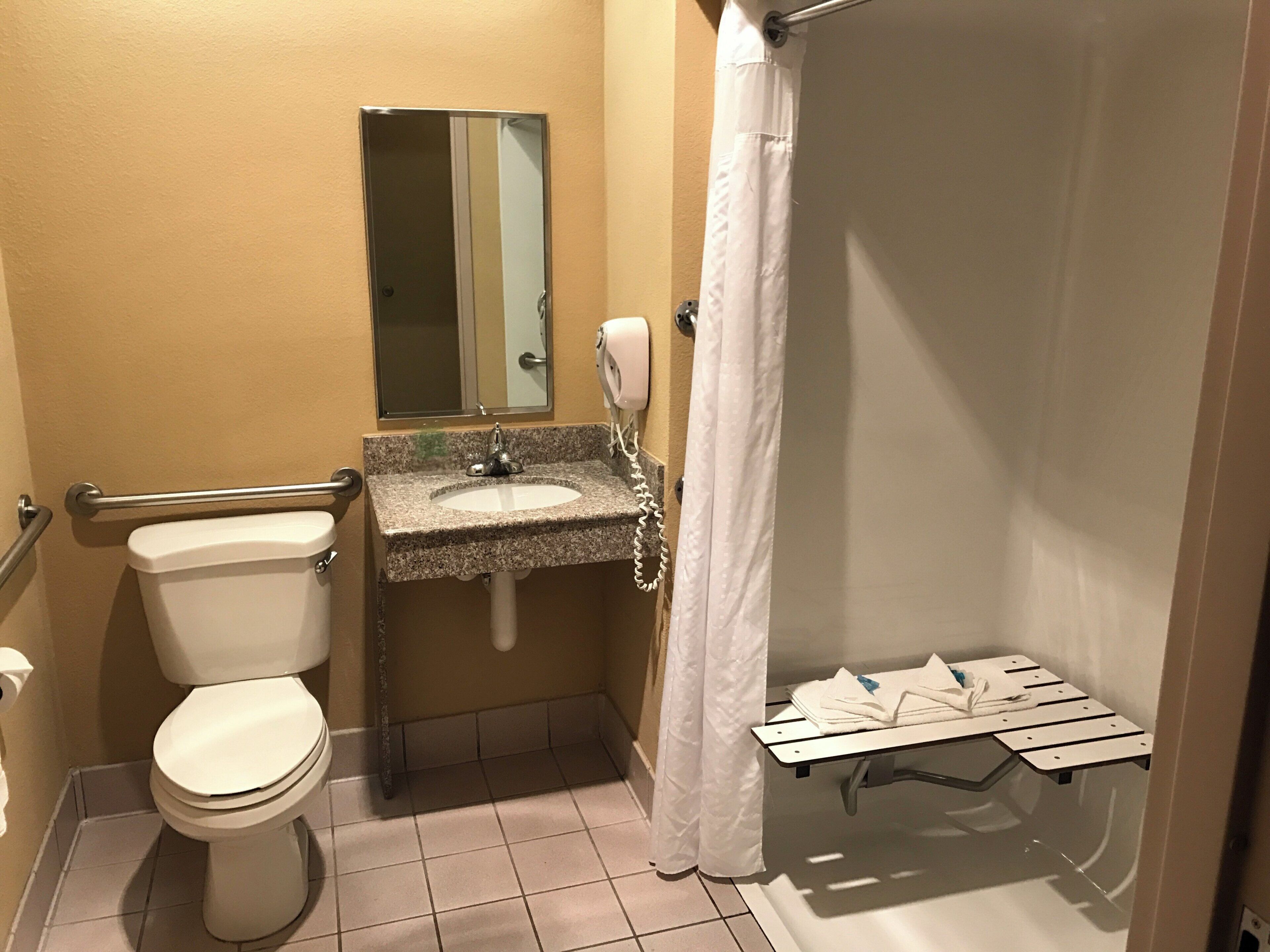 A bathroom with a toilet, sink, mirror, and shower area.