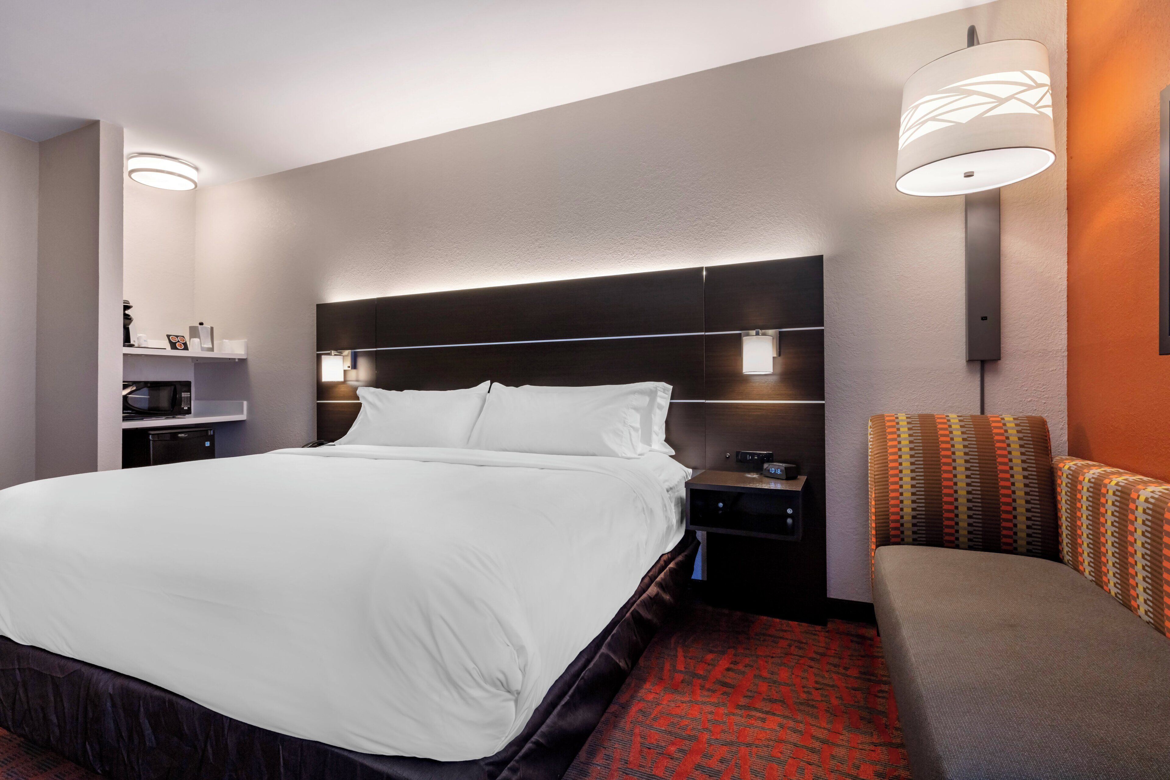 A hotel room with a large bed, bedside tables, a nightstand, a lamp, and a patterned sofa.