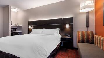 A hotel room with a large bed, bedside tables, a nightstand, a lamp, and a patterned sofa.