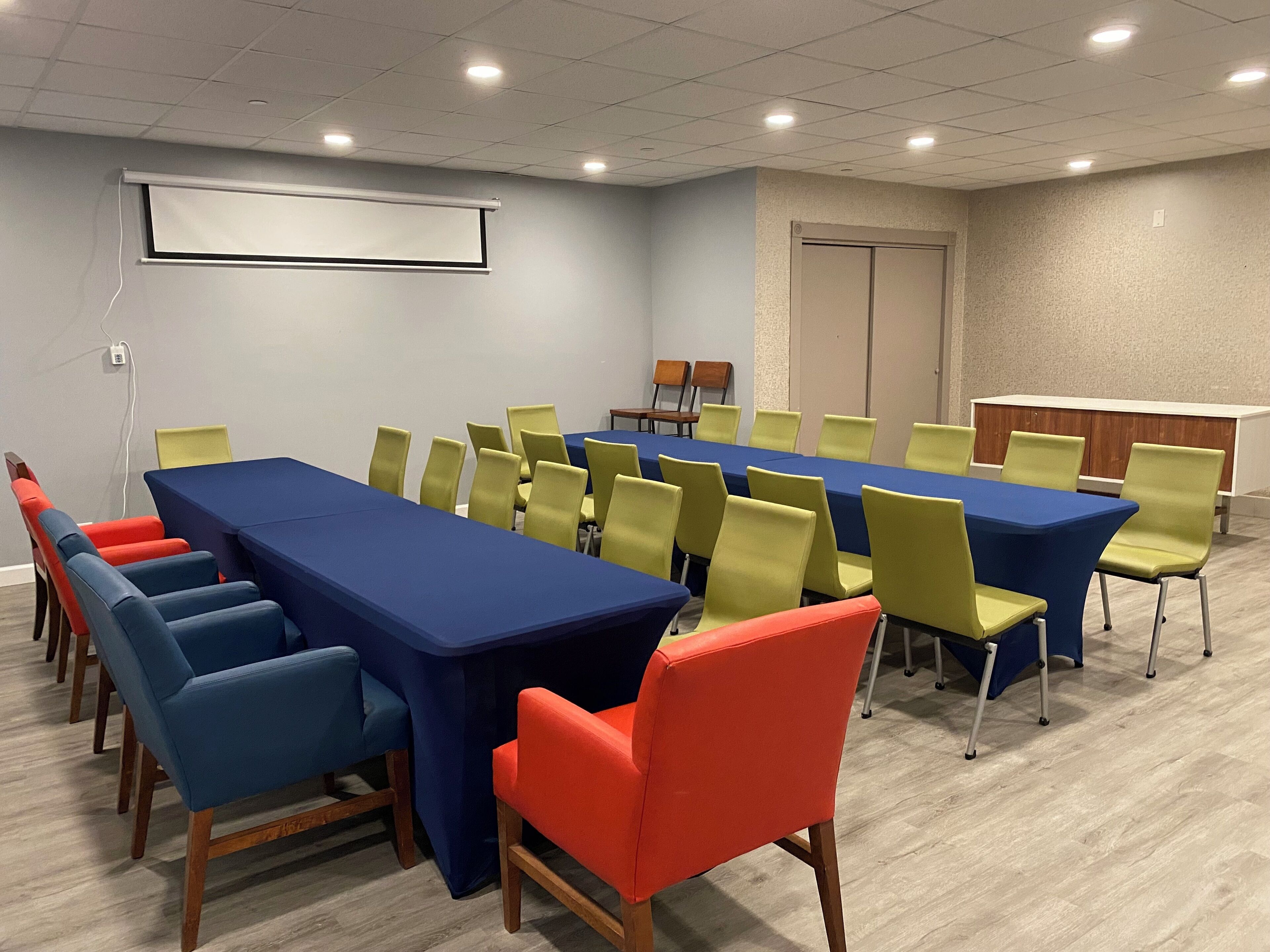 A conference room with a long table, multiple chairs, a projector screen, and a podium.
