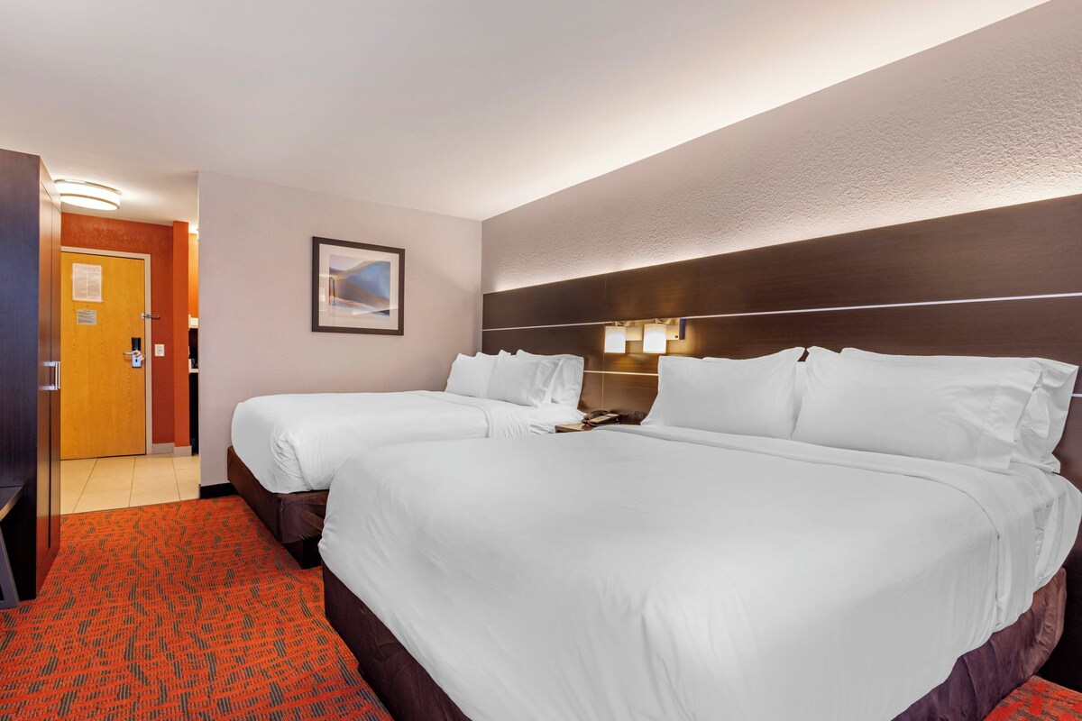 A hotel room with two beds, a wooden headboard, a framed picture on the wall, and a red carpet.
