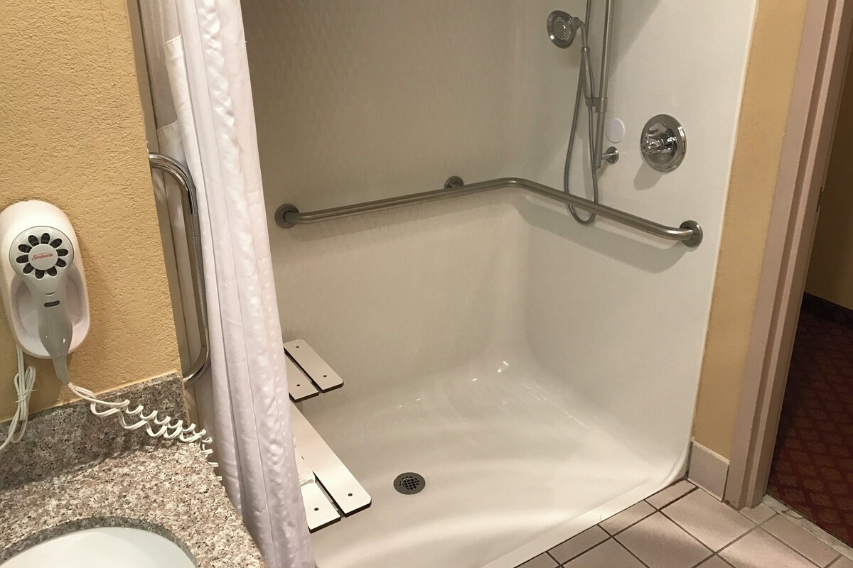 A shower area with a grab bar, a handheld showerhead, and a white sink with a countertop.