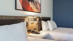 A hotel room with a bed, bedside table, and a wall-mounted artwork. - Hilton Garden Inn Chicago / Oak Brook (Villa Park)