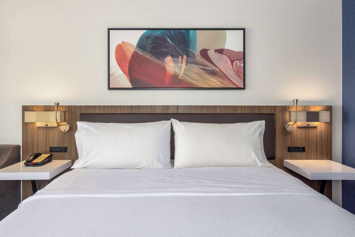 A hotel room with a large bed, two bedside tables, a telephone, and a wall-mounted abstract painting.