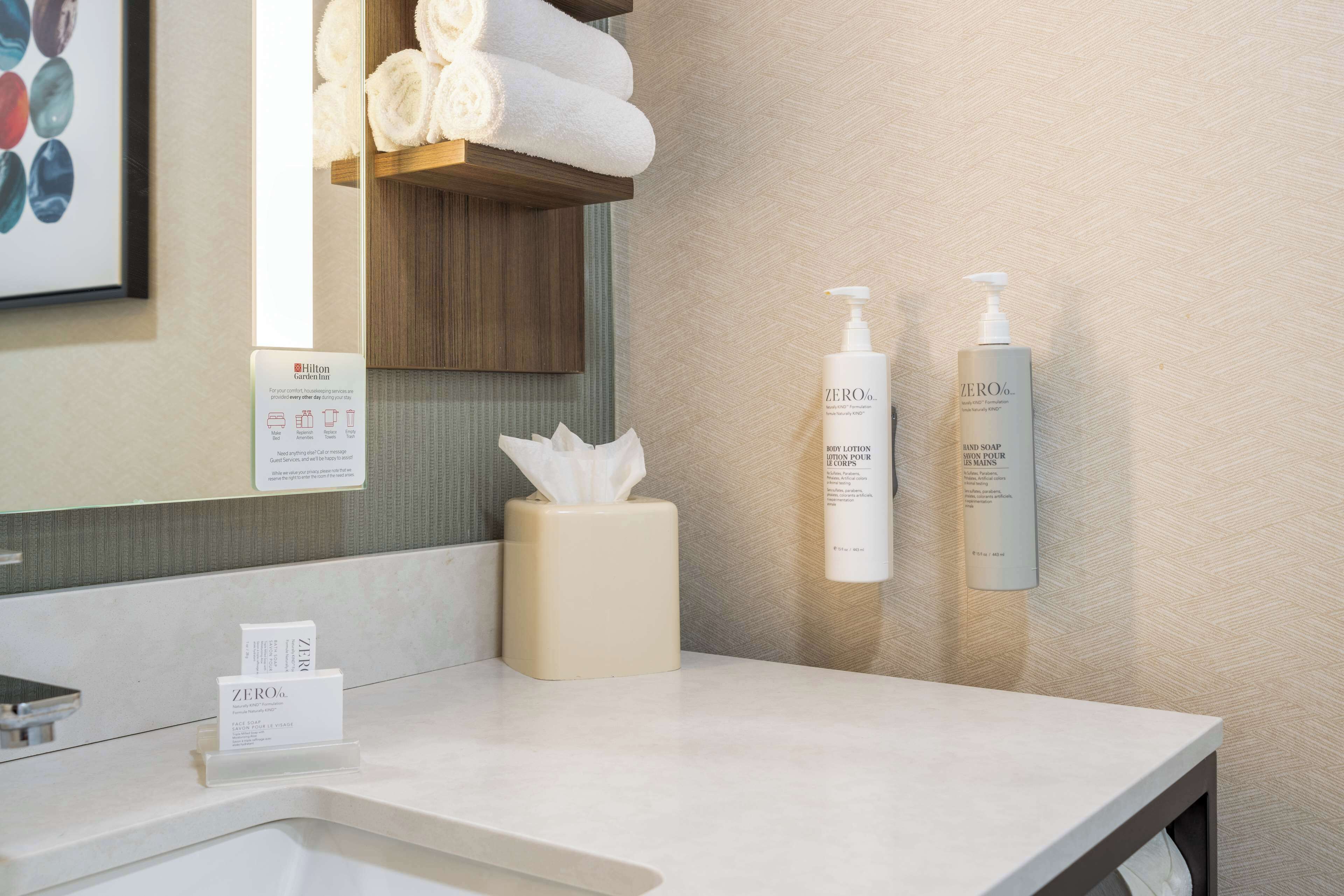 Een hotelbadkamer met een witte wastafel, een zakdoekdispenser en twee flessen ZERO® douchegel.