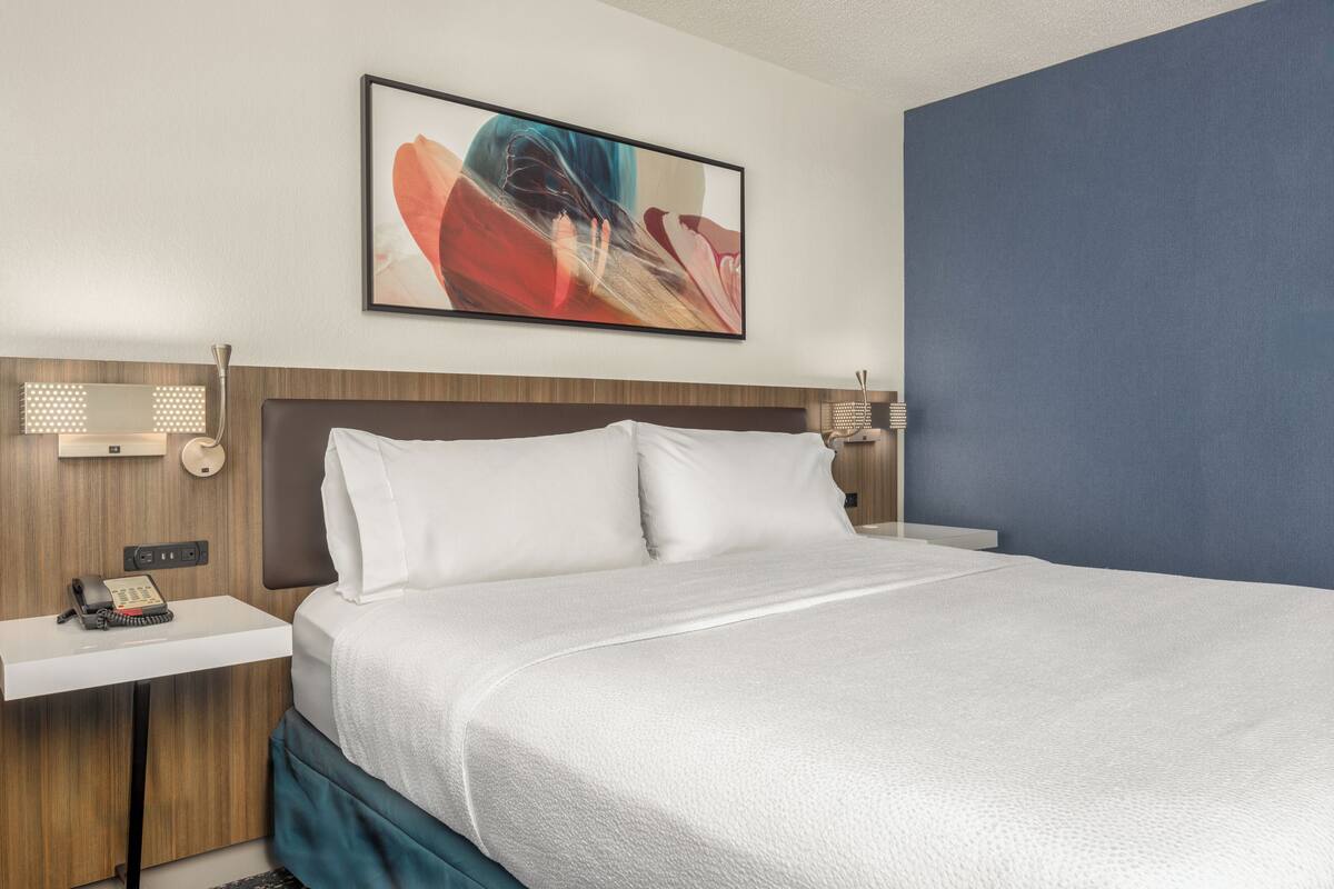 A neatly made bed with white linens, a wooden headboard, and a bedside table with a telephone.