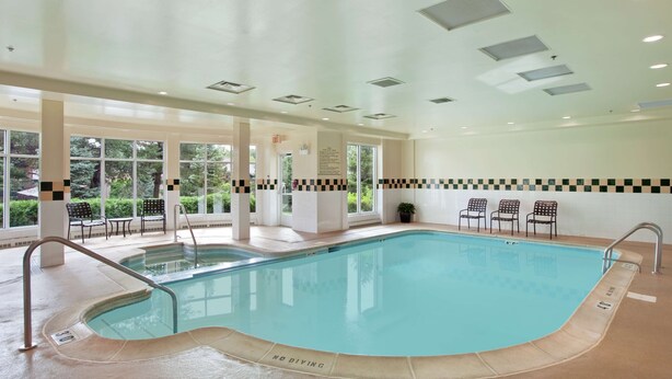 An indoor swimming pool with a 'NO DIVING' sign, seating area, and large windows. - Hilton Garden Inn Chicago / Oak Brook (Villa Park)