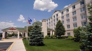 A multi-story hotel with a green lawn and flagpoles. - Hilton Garden Inn Chicago / Oak Brook (Villa Park)