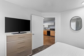 A hotel room with a bed, a TV, a dresser, a mirror, and a view into the kitchen. - MainStay Suites Chicago Schaumburg (Schaumburg)