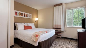 Habitación de hotel con cama, escritorio, televisor, ventana con cortinas y una pared decorada con obras de arte.