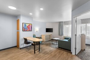 A hotel room with a dining area, a sofa, a TV, and a window with curtains. - MainStay Suites Chicago Schaumburg (Schaumburg)
