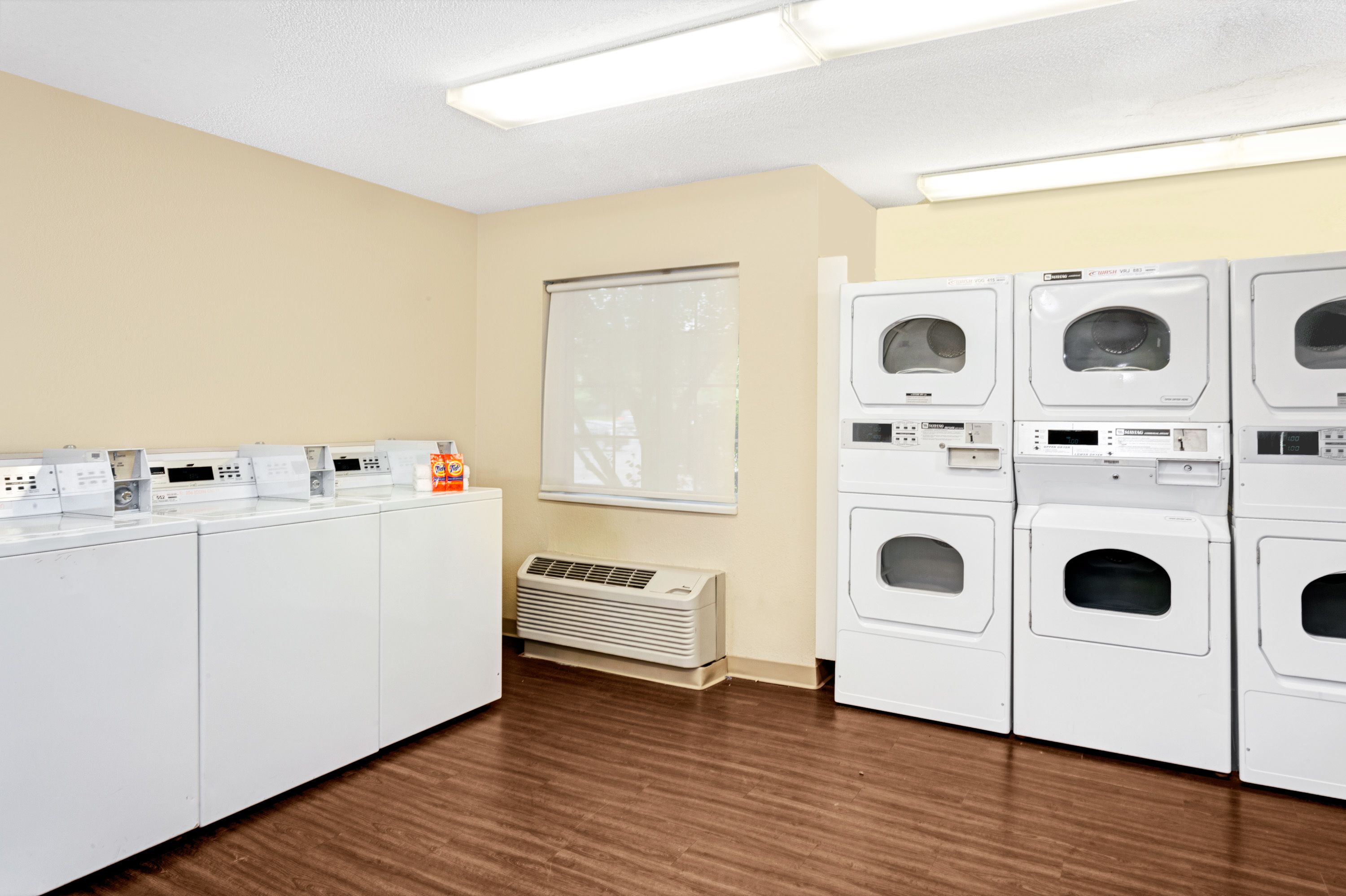 A laundry room with multiple washing machines and dryers, a window, and a vent.
