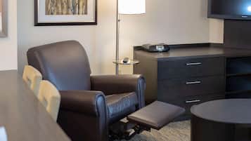 Habitación de hotel con sillón reclinable, una mesita, lámpara, televisor de pantalla plana y una cómoda.