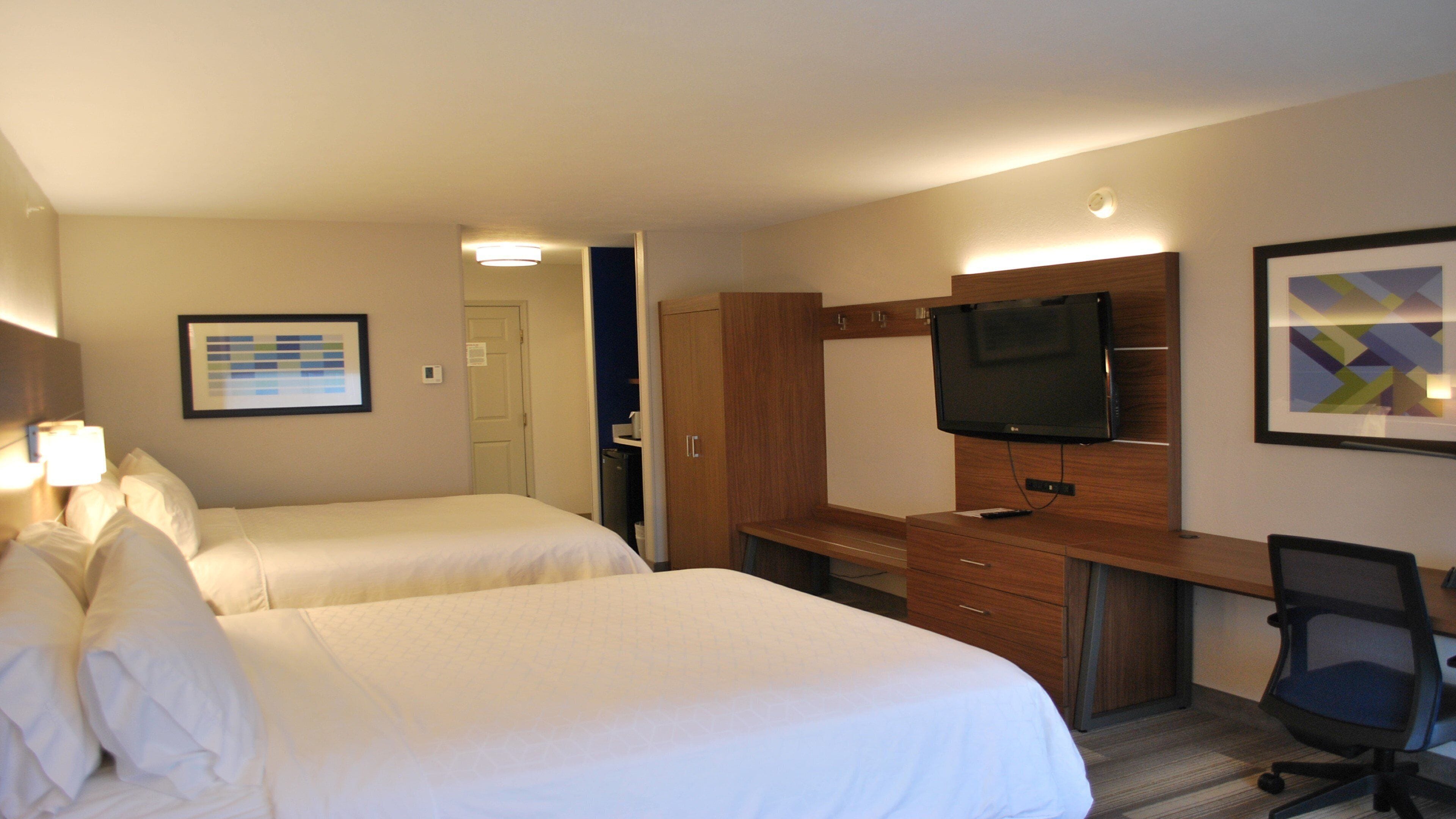 Quarto de hotel com duas camas, uma secretária com televisão, uma cadeira e um quadro na parede.