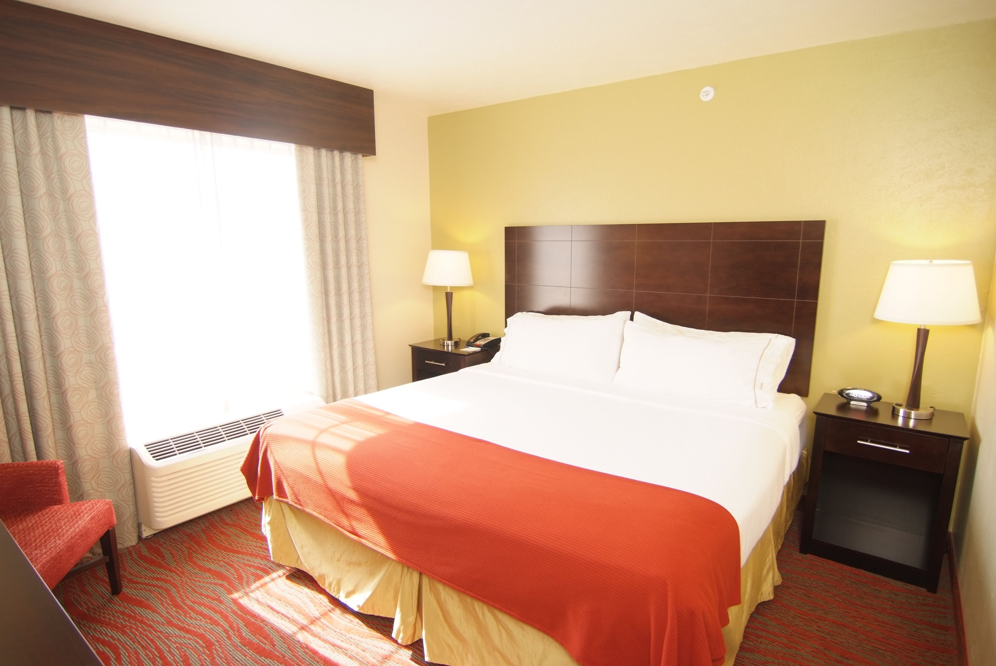 A hotel room with a large bed, two bedside tables with lamps, a chair, and a window with curtains.