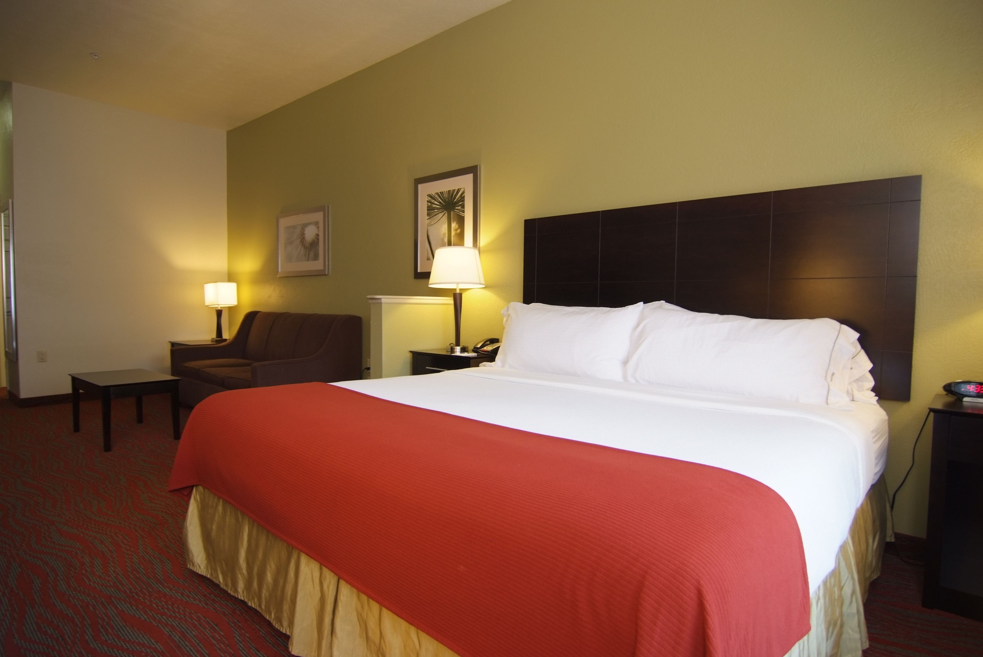 Habitación de hotel con una cama grande, una silla, una mesita de noche con lámpara y un cuadro en la pared.