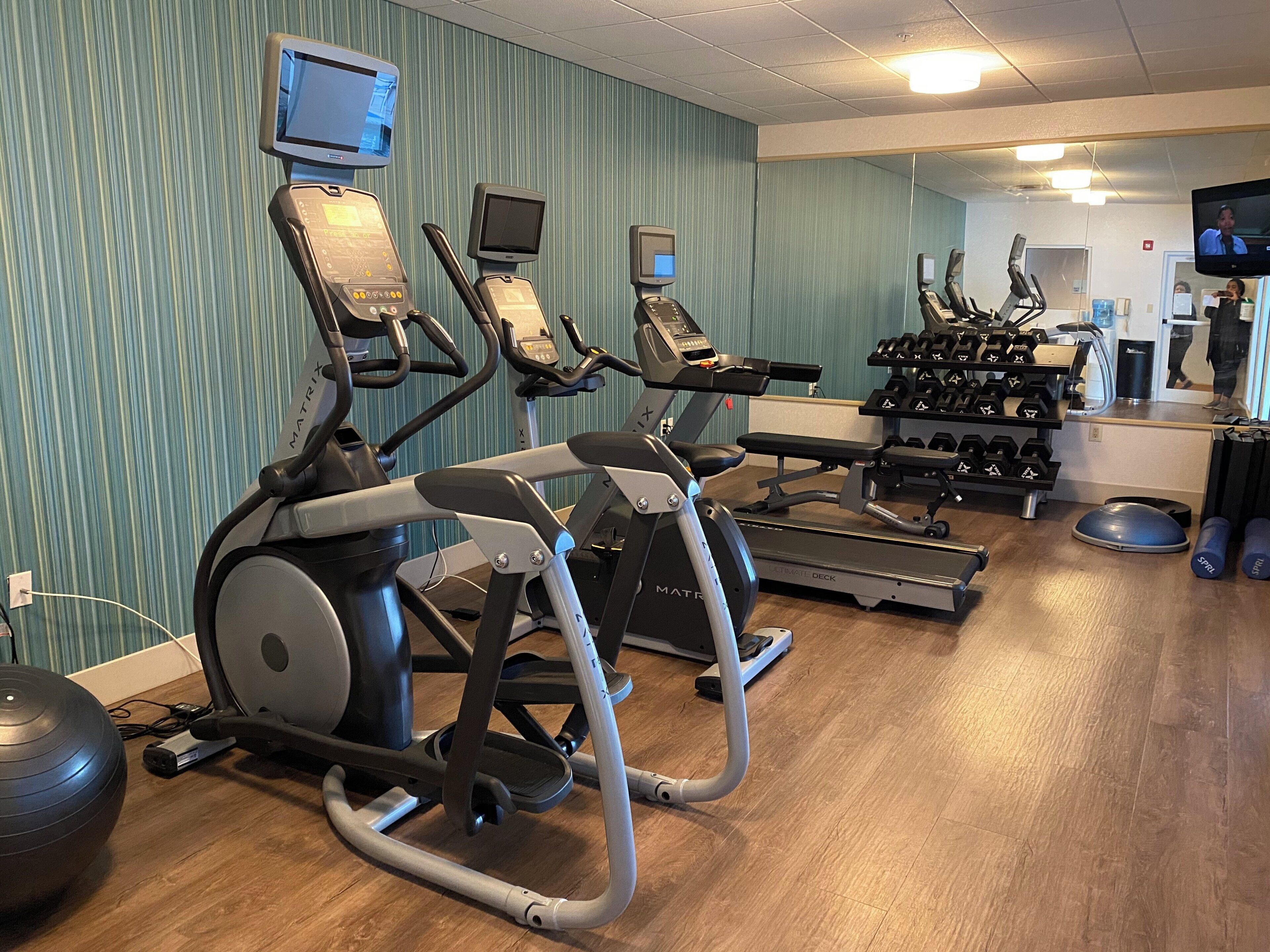 Un gimnasio con cintas de correr, elípticas y una zona de pesas.
