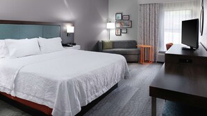A hotel room with a large bed, a desk, a TV, a sofa, and a small table. - Hampton Inn Jasper (Jasper)