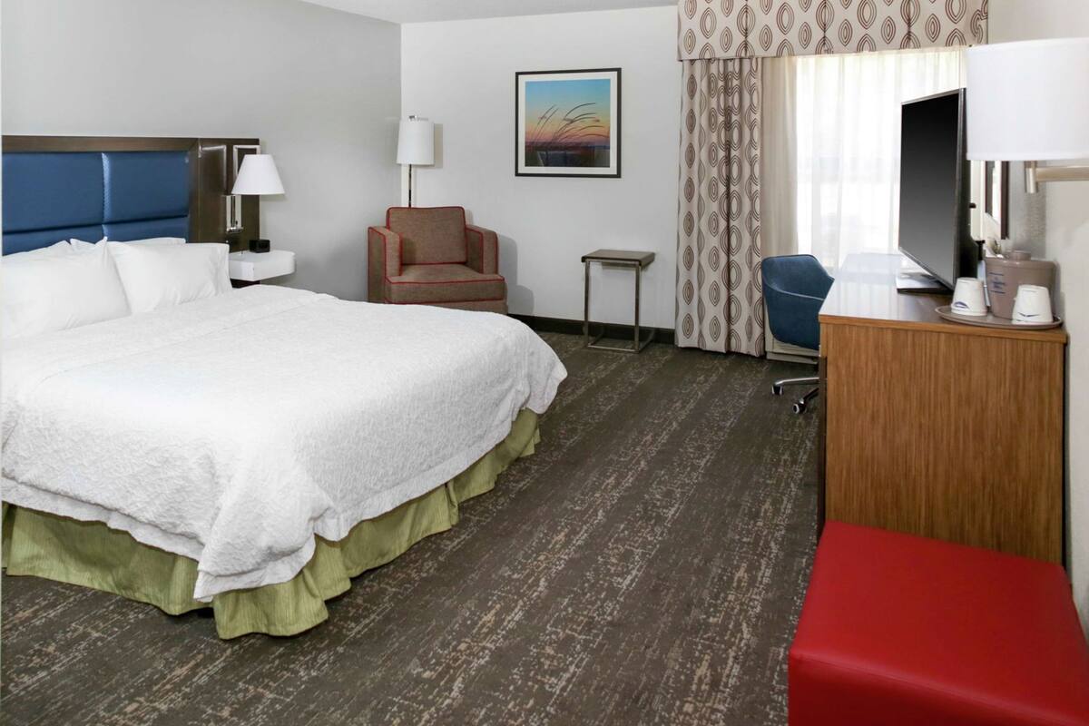 A hotel room with a large bed, a desk with a television, a chair, and a small table.