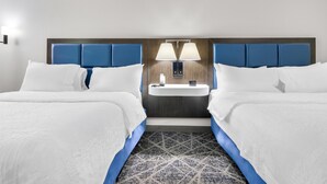 Una habitación de hotel con dos camas, una mesita de noche con una lámpara y un lavamanos pequeño.