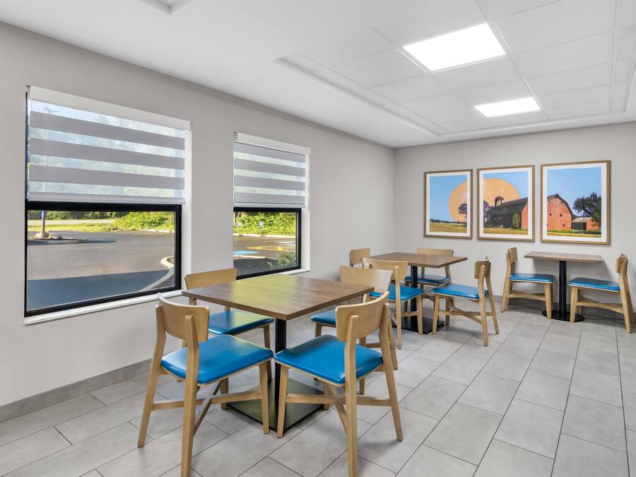 A dining area with tables and chairs, large windows, and artwork on the wall.