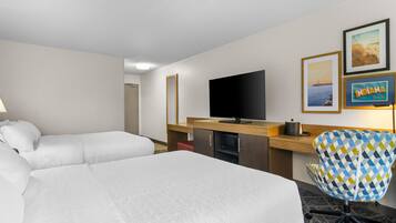 Quarto de hotel com duas camas, uma escrivaninha com televisão de tela plana, uma cadeira e obras de arte nas paredes.
