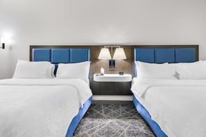 Una habitación de hotel con dos camas, una mesita de noche con una lámpara y un lavamanos pequeño.