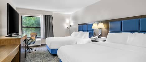A hotel room with two beds, a desk, a chair, a TV, and a window with curtains.