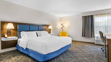 Quarto de hotel com uma cama grande, uma escrivaninha, uma cadeira e uma janela com cortinas.