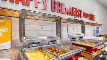Un bufé de desayuno con diversas opciones de comida y un cartel que dice 'HAPPY BREAKFAST STARTS HERE'.