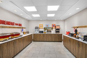 A breakfast area with a sign indicating the start of breakfast, a coffee machine, and a waffle maker.
