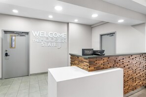 A hotel reception area with a modern design, featuring a reception desk with a wooden accent, a 'Welcome to the Hoosier State' sign, and a 'Hilton Honors' sign. - Hampton Inn Portage (Portage)