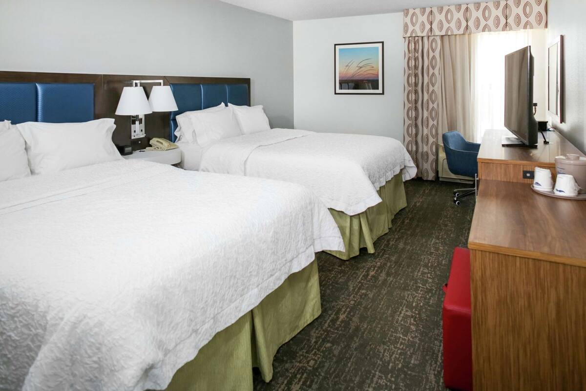 A hotel room with two beds, a desk, a chair, a TV, and a painting on the wall.