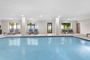 Una piscina con sillas de descanso y una puerta que da a una zona techada.
