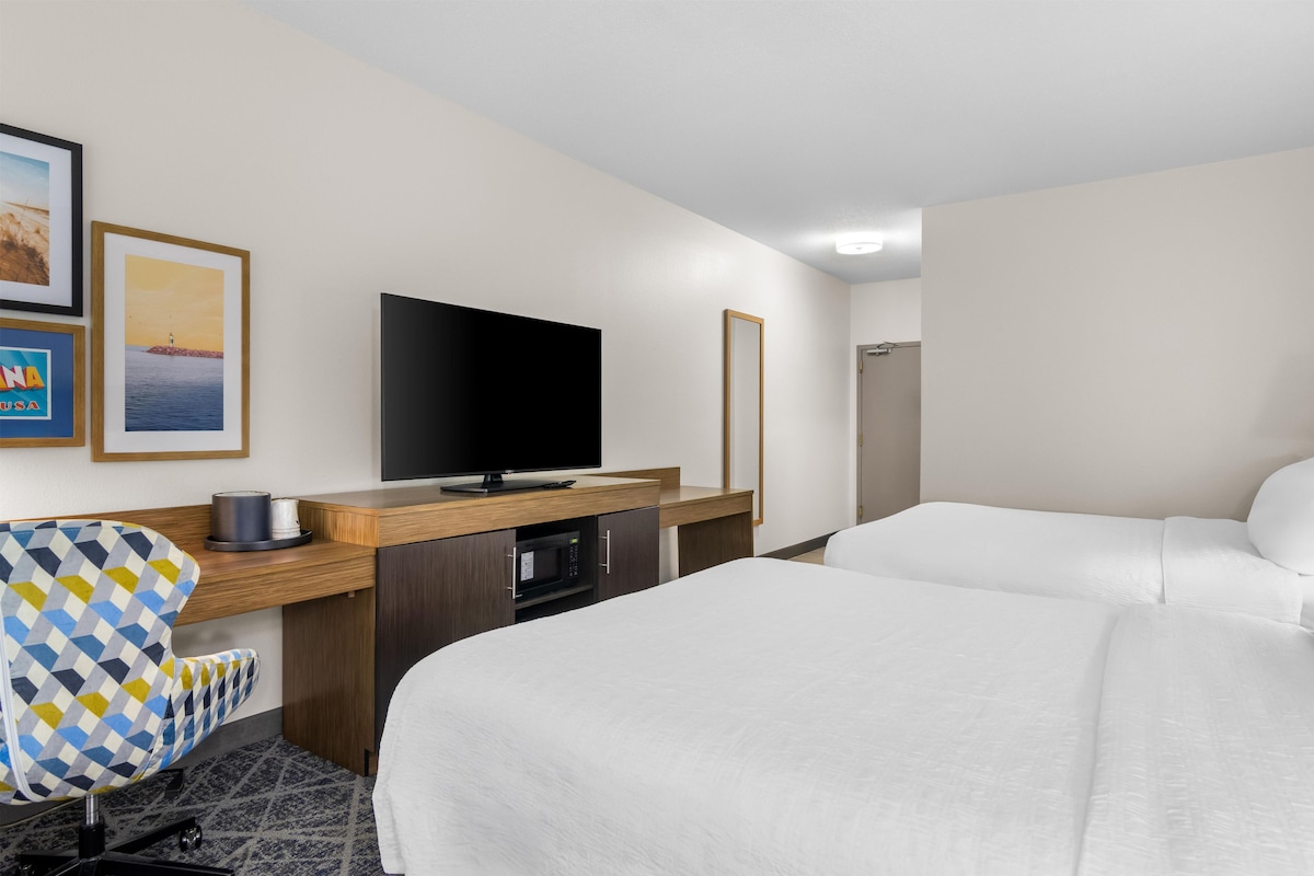A hotel room with a bed, a desk with a flat-screen TV, a microwave, and a chair.