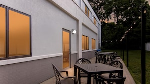 Un patio al aire libre con mesas y sillas, un edificio con ventanas grandes y luces colgantes.