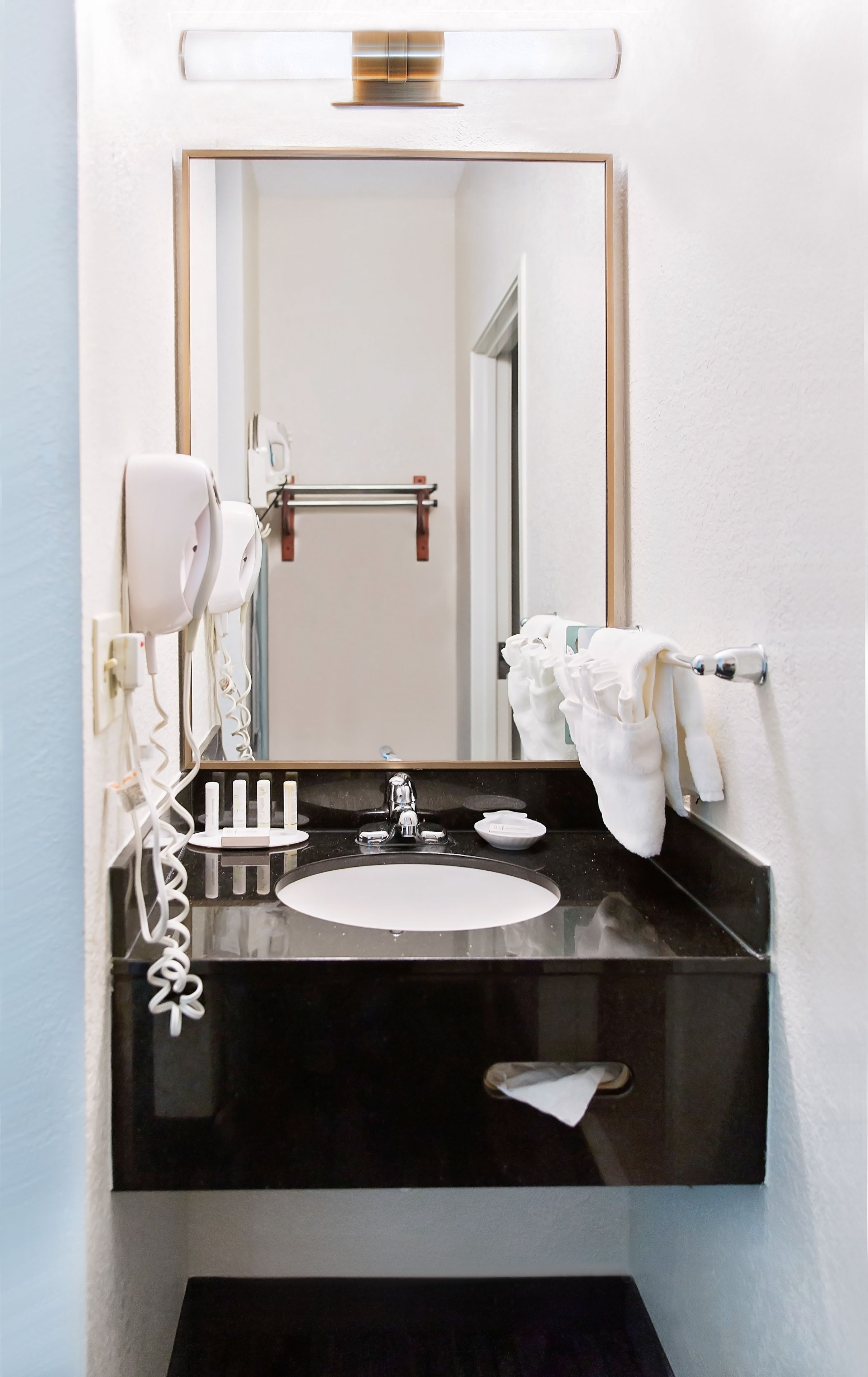 Un baño moderno con un lavamanos negro, accesorios blancos, un secador de pelo y un perchero para toallas.