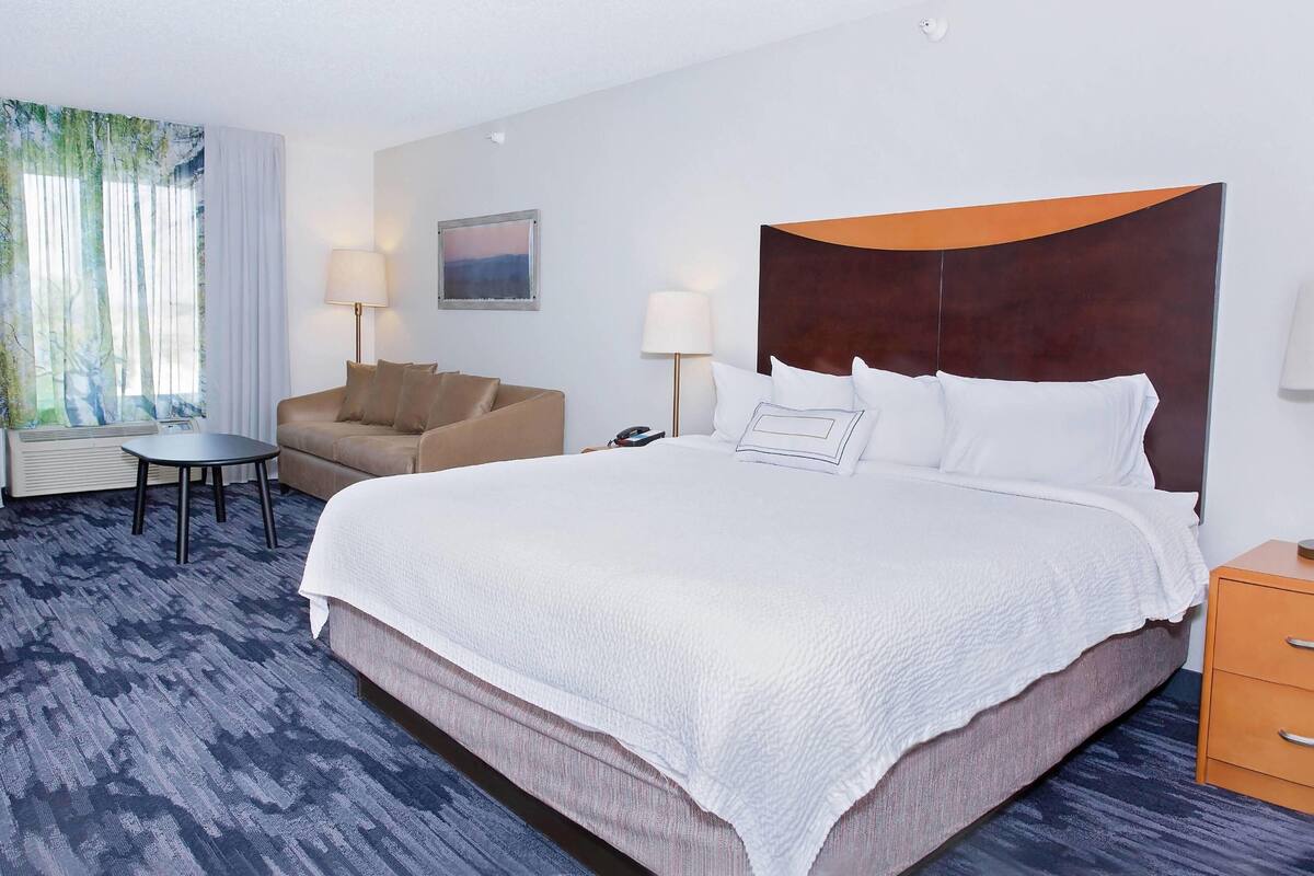 A hotel room with a large bed, a sofa, a small table, and a nightstand.