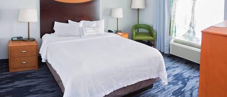 Une chambre d’hôtel avec un grand lit, deux tables de chevet avec des lampes, un fauteuil vert et une fenêtre avec des rideaux.