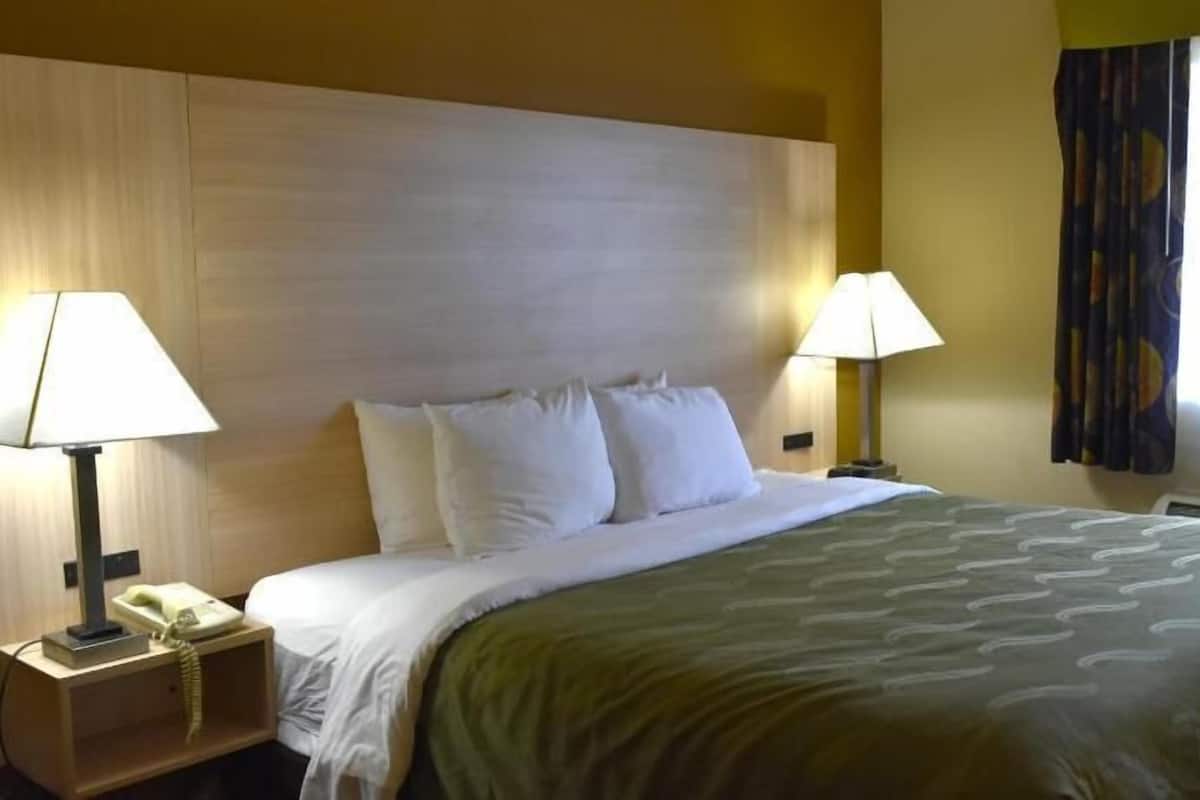 Quarto de hotel com cama, duas luminárias de cabeceira, telefone e janela com cortinas.