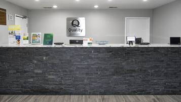 A hotel reception desk with a dark stone counter, a sign reading 'Quality by Choice Hotels', and a computer monitor displaying 'WELCOME!'.