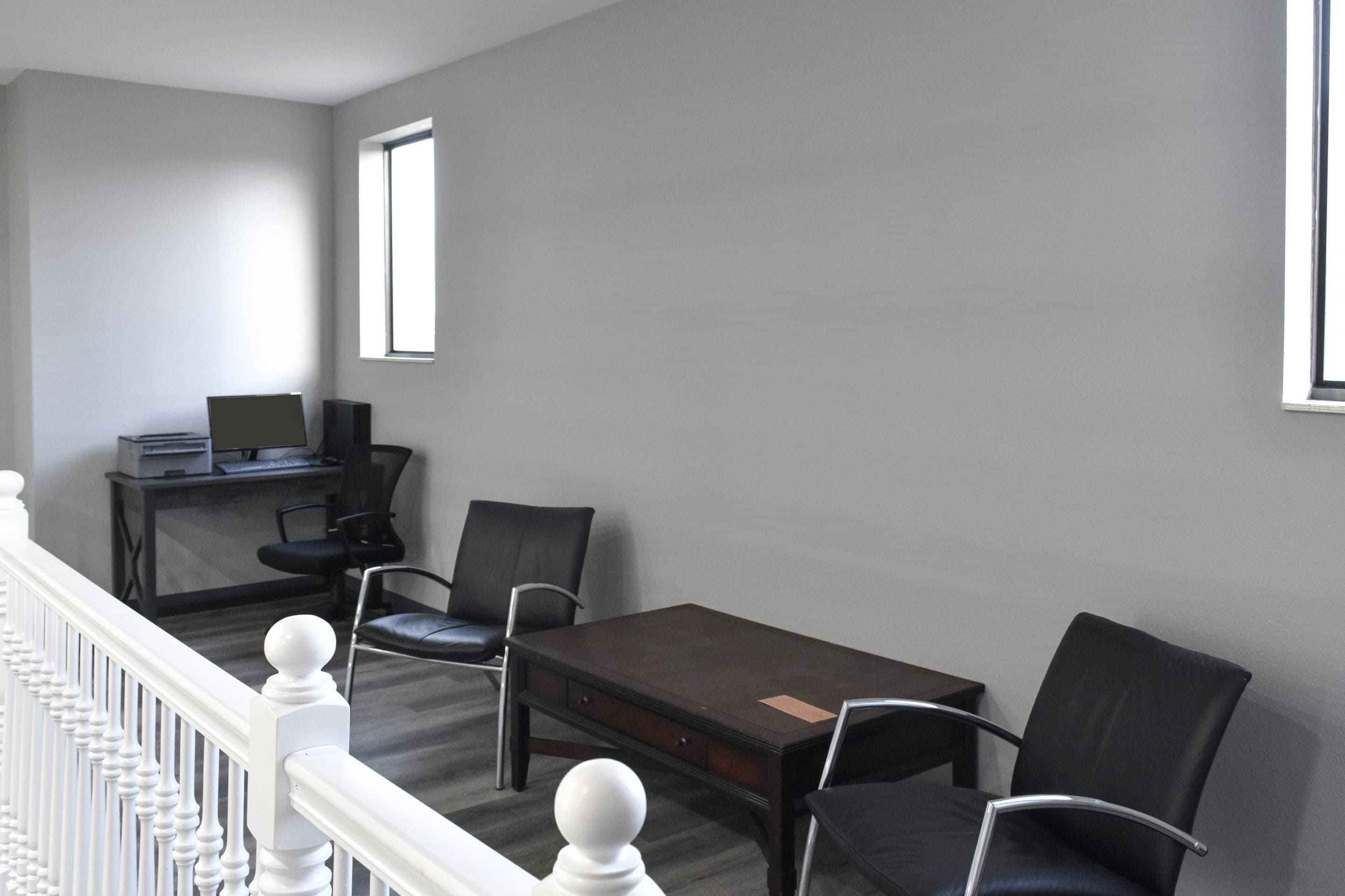A room with a desk, two chairs, a computer, and a window.