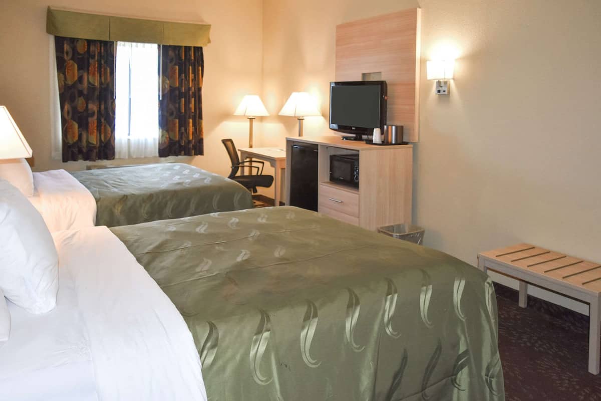 Quarto de hotel com duas camas, uma mesa de trabalho com televisão e micro-ondas.