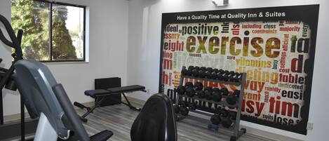 Une salle de sport équipée de matériel d’exercice, un mur orné de citations motivantes et une fenêtre donnant sur un paysage arboré.