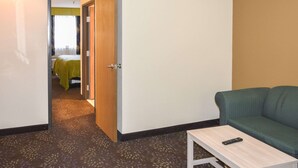Ein Hotelzimmer mit einem grünen Sofa, einem kleinen Tisch mit einer Fernbedienung und einer Tür zu einem Badezimmer mit einem gelben Handtuch.