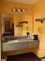Baño de hotel con encimera de granito, espejo, secador de pelo y toallero.